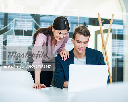 Young businessman and businesswoman using laptop at table in office
