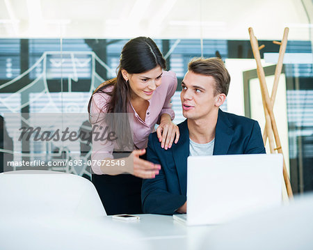 Young businessman with female colleague discussing over laptop at table in office