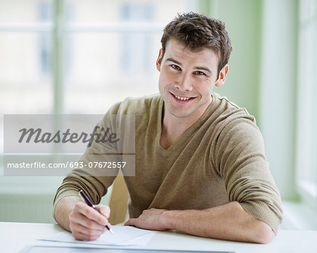 Portrait of handsome businessman writing on document at desk in office