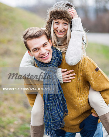 Portrait of happy man piggybacking woman in park