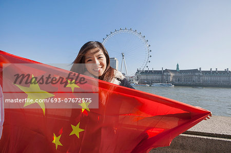 Portrait of happy young woman holding Chinese flag against London Eye at London, England, UK