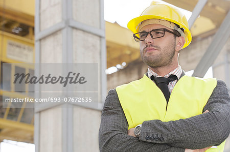 Young male architect standing arms crossed at construction site