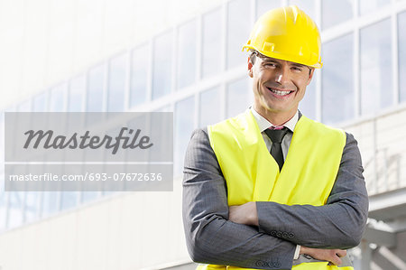 Portrait of smiling young male architect standing arms crossed outside office building