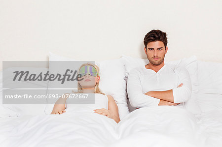 Portrait of displeased man with woman sleeping in bed