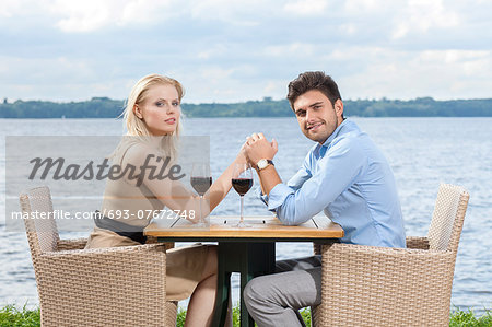 Side view portrait of young couple holding hands at outdoor restaurant by lake