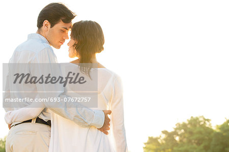 Rear view of romantic couple standing arms around against clear sky