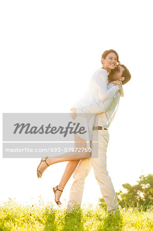 Side view of man lifting woman in park against clear sky