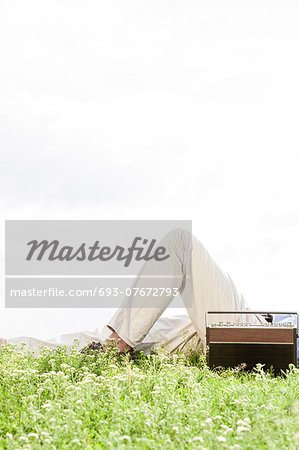 Midsection of man lying by vintage radio on grass against clear sky
