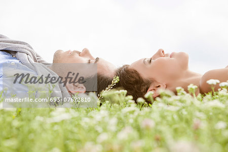 Side view of young couple sleeping on grass against clear sky