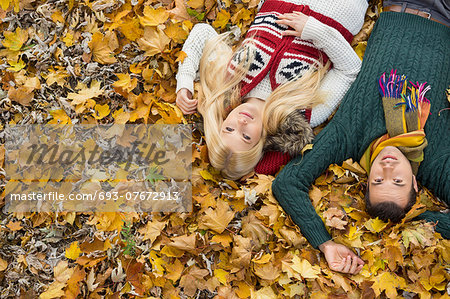 High angle portrait of young couple lying on autumn leaves at park