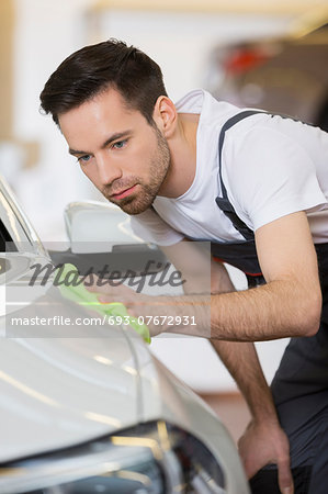 Young maintenance engineer cleaning car in repair shop