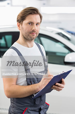 Portrait of confident automobile mechanic writing on clipboard in workshop Portrait of confident automobile mechanic writing on clipboard in workshop