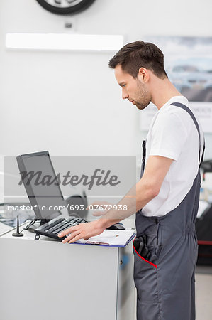 Side view of automobile mechanic using computer in workshop