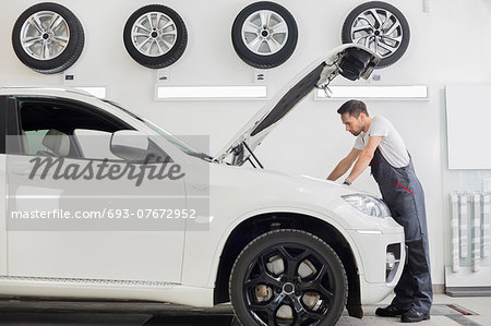 Full length side view of male mechanic examining car engine in repair shop