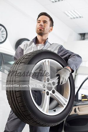 Young maintenance engineer carrying tire in automobile store Young maintenance engineer carrying tire in automobile store