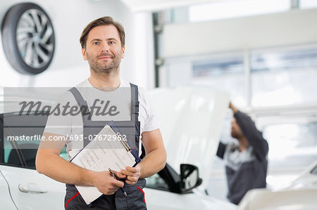 Portrait of confident male maintenance engineer with clipboard in car repair shop