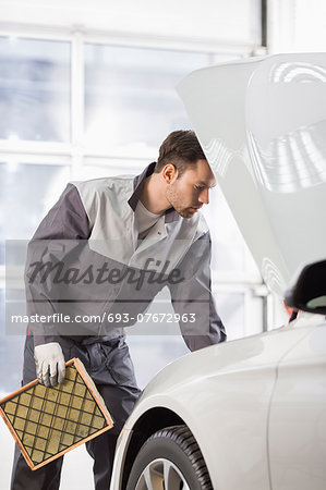 Young automobile mechanic examining car in automobile shop