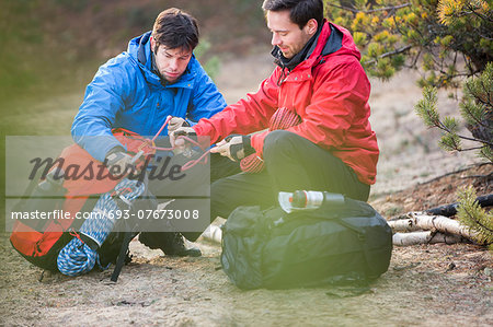 Male backpackers looking at rope in forest