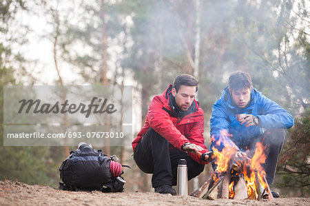 Male hikers warming hands at campfire in forest