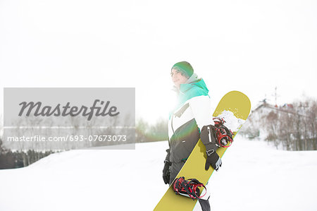 Young man with snowboard walking in snow