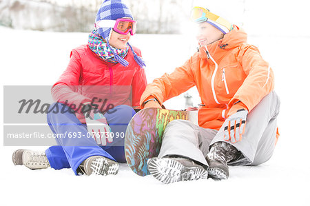 Full length of female friends with snowboard relaxing on snow