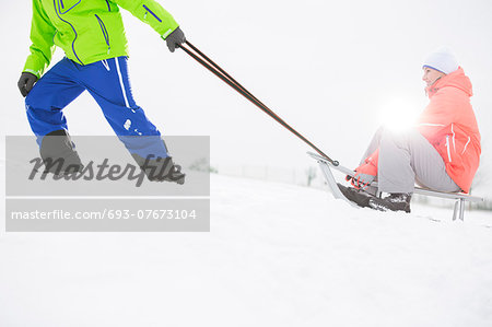 Low section of man giving sled ride to woman in snow