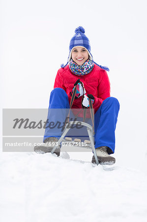Full length portrait of happy young woman enjoying sled ride in snow