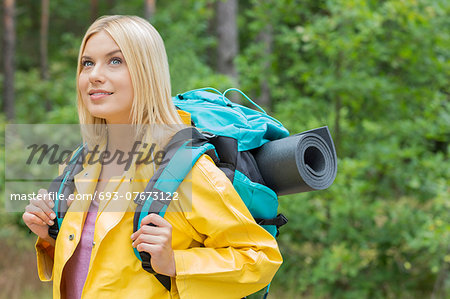 Smiling female backpacker in raincoat looking away at forest