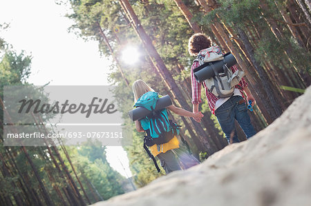 Rear view of hiking couple holding hands while walking in forest