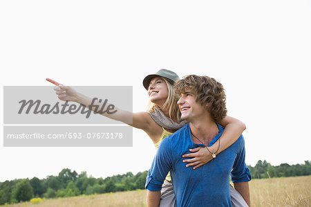 Happy woman showing something while enjoying piggyback ride on man in field