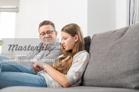 Father and daughter using digital tablet on sofa at home