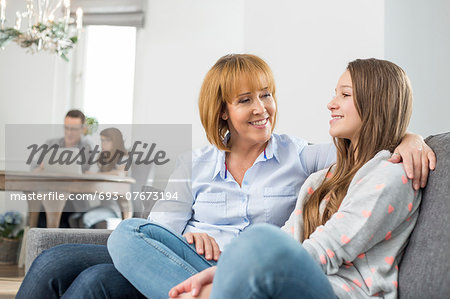 affectionate mother and daughter sitting on sofa with family in background