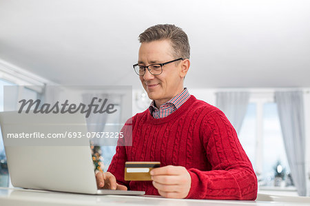 Mature man using credit card and laptop to shop online during Christmas