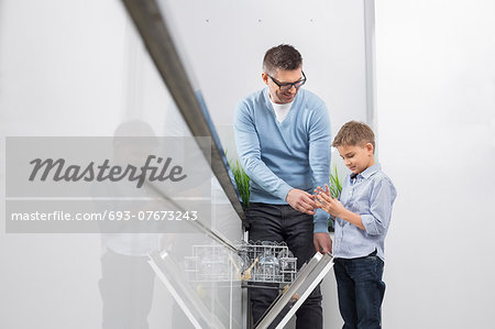 Father and son placing glass in dishwasher at kitchen