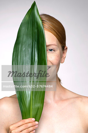 Young woman holding up leaf concealing part of face