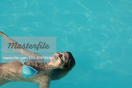 Woman floating in pool, eyes closed, high angle view