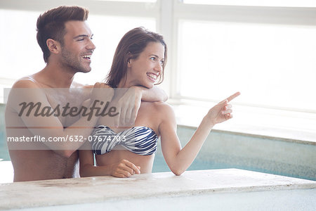 Couple wading in indoor pool looking at view through window