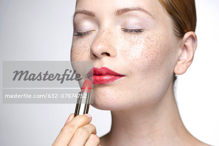 Young woman putting on lipstick