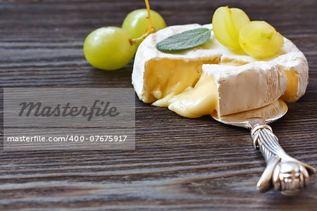 Round Camembert cheese with a section cut out and served grape and leaf of sage.