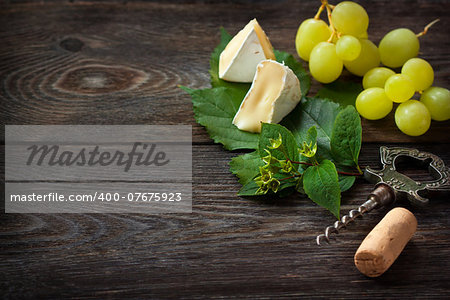 Delicious cheese and ripe grape with wine cork and corkscrew on an old wooden board. Vintage style.