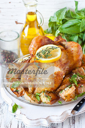 Whole roasted chicken with baked potatoes, lemon and thyme on a pan close-up. Rustic style.