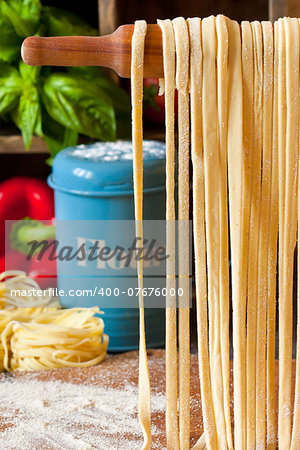 Fresh homemade pasta hanging on wooden rolling pin close-up.