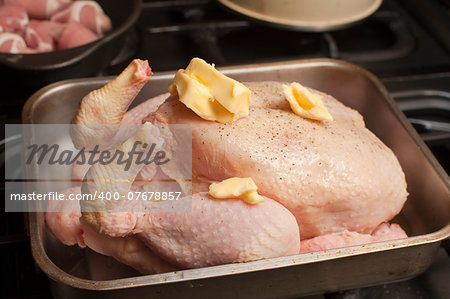 Uncooked seasoned turkey topped with dollops of butter in a roasting pan or oven dish waiting to be placed in the oven for roasting