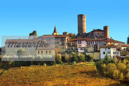 Yellow vineyards and small medieval town on the hill in autumn in Piedmont, Northern Italy.
