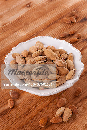 Almonds in white vintage bowl on wooden background. Healthy nuts eating.