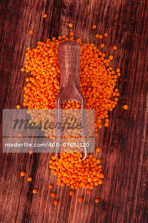 Red lentils on wooden spoon on dark wooden background. Healthy legume eating.