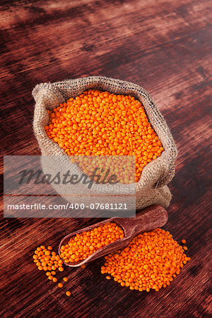 Red lentils in burlap sack with wooden spoon on dark wooden background. Healthy cooking.