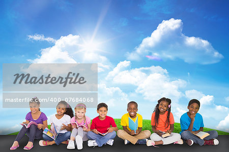 Cute pupils smiling at camera with books against green hill under blue sky