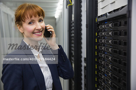 Smiling technician talking on phone while looking at server in large data center