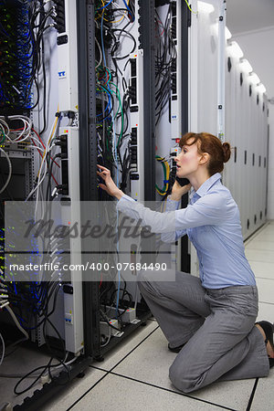 Serious technician talking on phone while analysing server in large data center
